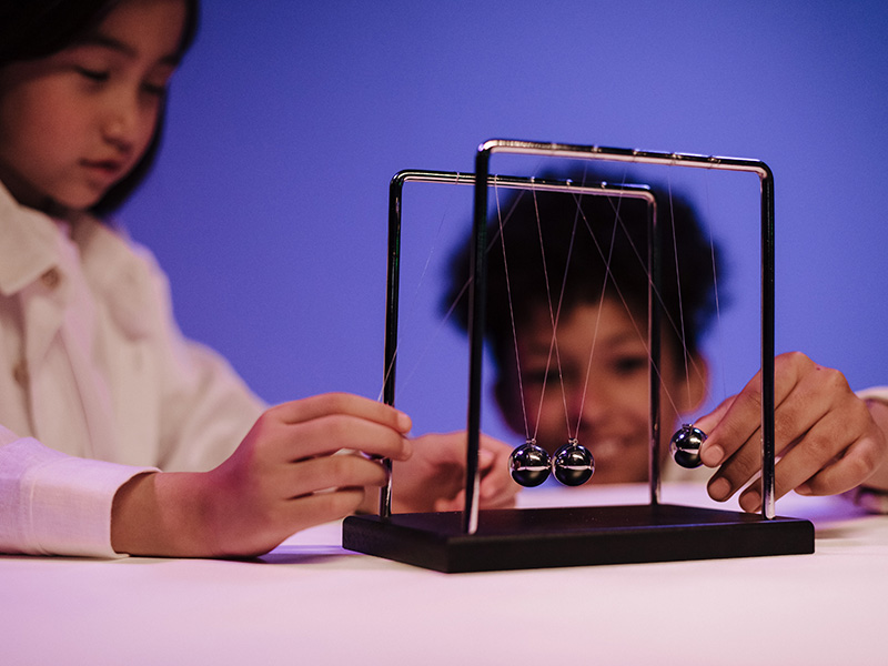 two kids playing with Newtons cradle, demonstrating motion-physics