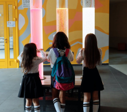 three girls looking into three big sylinders with colored liquid